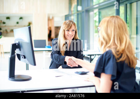 Screenshot des mittleren Alters geschäftsfrau am Schreibtisch sitzen und die Hände schütteln mit ihrer Kollegin. Stockfoto