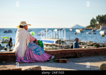 Lokale Frau tragen schicke Kleidung und Sitzen am Strand von Copacabana, Bolivien Stockfoto