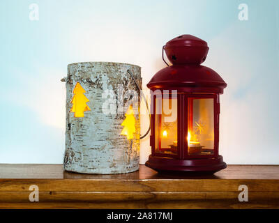 Advent Laternen. Zwei Laternen nebeneinander stehend auf dem Holzbrett. Warmes Licht von Kerzen, weiße Wand hinter sich. Stimmung der Ruhe und Wärme. Stockfoto