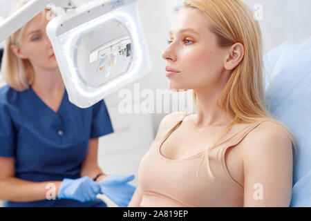 Kosmetologie Service. Junge Frau von Schönheit Klinik in der Nähe sitzen - bis nachdenklich, während Ihr Arzt untersuchen Stockfoto