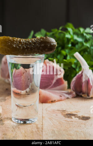 Geschnittenem gekochtem Schweinefleisch auf einer Tafel mit Petersilie, Knoblauch und ein Glas Wodka mit Gurke Stockfoto