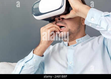 Freestyle. Junge Menschen in der virtuellen Realität headset Studio sitzen auf einem Sofa auf Grau spielen Beißen Nägel isoliert nervös Stockfoto