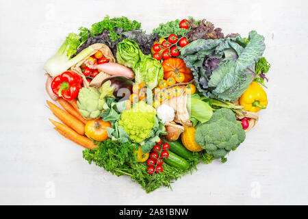 Gesunde Ernährung Konzept. Rainbow Gemüse in einer Form des Herzens auf weissem Holztisch Tomaten Kohl Grüns Möhren Brokkoli, Ansicht von oben, auf weissem Holztisch, selektiver Fokus Stockfoto