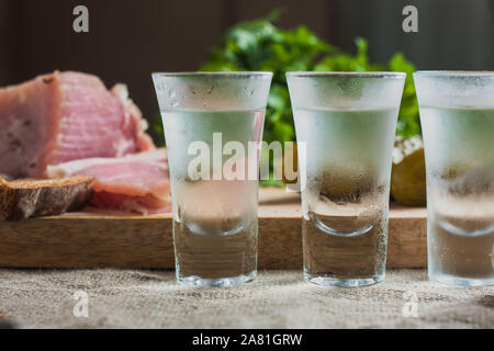 Freundlich Schnäpse - drei Gläser Wodka auf dem Tisch vor dem Hintergrund der Snacks - Schmalz, Knoblauch, Petersilie, Brot, Gurke Stockfoto