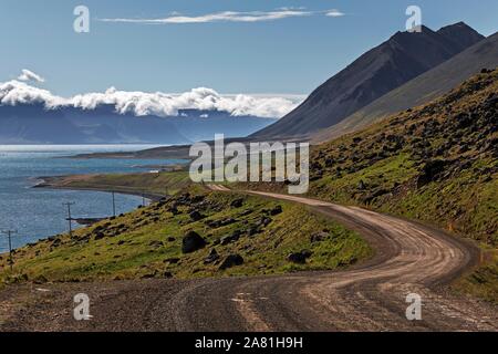 Schotterstraße schlängelt sich entlang einem Fjord durch vulkanische Landschaft, in der Nähe von Hrafnseyri, Westfjorde, Island Stockfoto