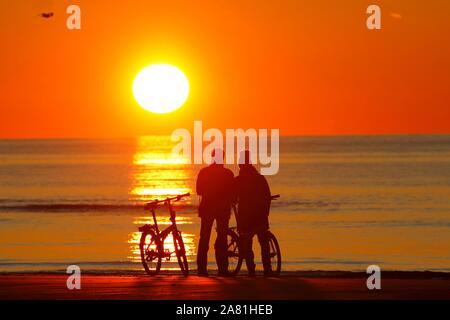 Paare mit Fahrrädern am Strand den Sonnenuntergang beobachten, Nordsee, St. Peter-Ording, Nordseeküste, Nationalpark Schleswig-Holsteinisches Wattenmeer Stockfoto