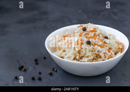 Hausgemachten Sauerkraut mit Karotten in einer Schüssel auf einem dunklen Hintergrund, fermentierte Lebensmittel, Nahaufnahme Stockfoto