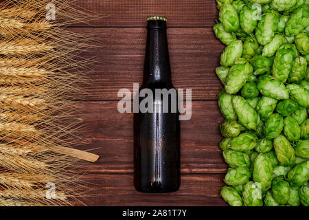 Ein Glas Flasche Bier, grüne Kegel von Hopfen und Getreide auf Holz- Hintergrund. Ansicht von oben. Freier Platz für Text. Stockfoto