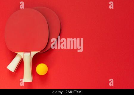 Rot Tennis ping pong Schläger und orange Kugel auf einem roten Hintergrund isoliert, Sport Ausrüstung für Tischtennis Stockfoto