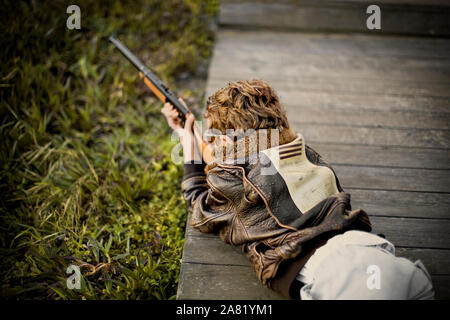 Junge, das darauf abzielt, eine Schrotflinte beim liegen auf dem Bauch auf einem Holzsteg. Stockfoto