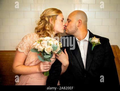 Nahaufnahme von Braut und Bräutigam in Vintage Kleidung sitzen und berühren und Küssen mit Braut holding Blumenstrauß warten zu heiraten Stockfoto