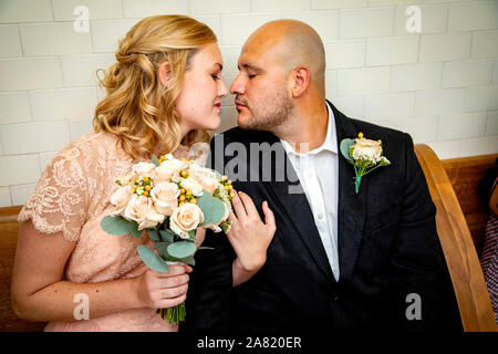 Nahaufnahme von Braut und Bräutigam in Vintage Kleidung sitzen und berühren und Küssen mit Braut holding Blumenstrauß warten zu heiraten Stockfoto