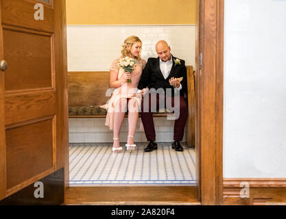 Bild von Paar sitzen und mit geradem Mann an der Heiratsurkunde im Vintage Style Courthouse suchen schoss durch Tür Stockfoto