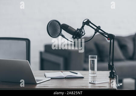 Mikrofon, Laptop, Notebook und Glas Wasser auf hölzernen Tisch in Rundfunk und Studio Stockfoto