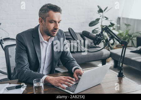 Stattliche radio Host mit Laptop, während am Arbeitsplatz in der Nähe von Mikrofon sitzen Stockfoto