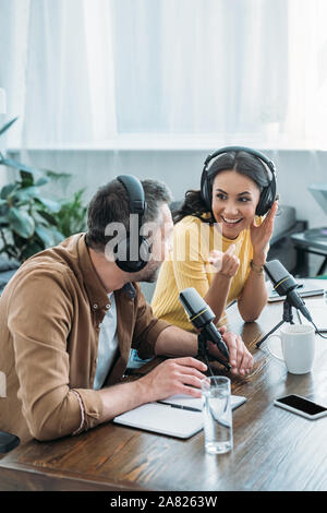 Hübsches radio Host lächelnd und deutete während der Aufnahme podcast mit Kollegen Stockfoto