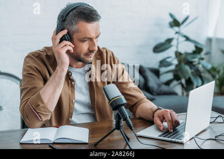 Aufmerksame radio Host in Kopfhörer mit Laptop, während in der Nähe von Mikrofon sitzen Stockfoto