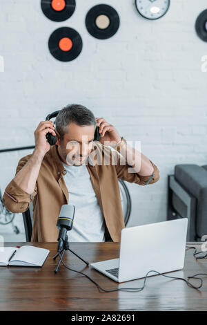 Stattliche radio host Holding setzen auf Kopfhörer und Notebook suchen Stockfoto