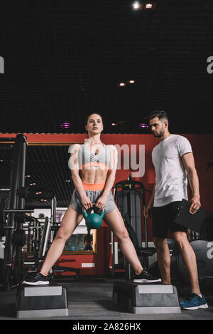 Aufmerksame trainer Überwachung junge Sportlerin heben Gewicht in der Turnhalle Stockfoto