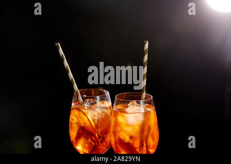 Aperol Spritz in Gläsern mit Strohhalmen auf schwarzem Hintergrund Stockfoto