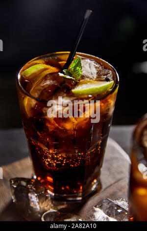 Selektiver Fokus der Cocktail cuba libre in Glas mit Stroh, Eiswürfel auf schwarzem Hintergrund Stockfoto