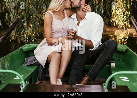 7/8-Ansicht von glückliches junges Paar küssen beim Sitzen im Boot auf dem See Stockfoto