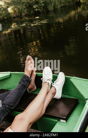 7/8-Ansicht der Barefoot Mann und Mädchen in Turnschuhen entspannen im Boot auf dem See Stockfoto