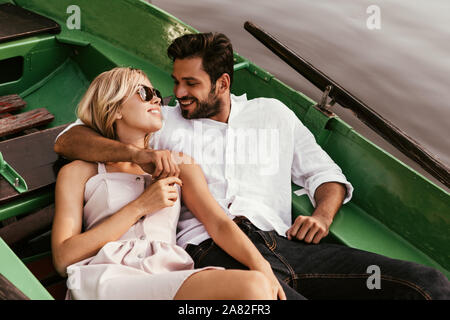 Glückliche junge Mann umarmt hübsche Freundin, während im Boot sitzen Stockfoto
