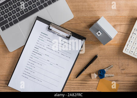 Blick von oben auf die Zwischenablage mit Property management Vereinbarung, Haus Modell, Laptop, Tasten und Stift auf hölzernen Schreibtisch Stockfoto