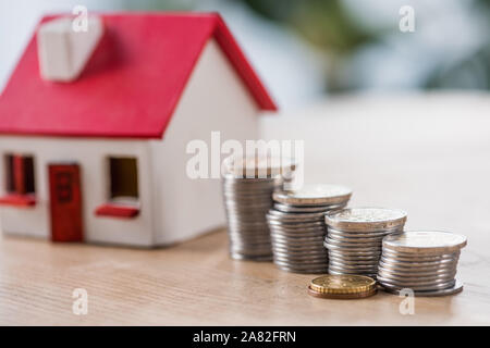 Selektiver Fokus der sortierten silbernen und goldenen Münzen in der Nähe von Spielzeug Haus auf hölzernen Tisch Stockfoto