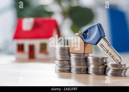 Selektiver Fokus der Schlüssel mit Spielzeug Haus Schmuckstück auf Stapel von Münzen, die in der Nähe von House Modell auf hölzernen Tisch Stockfoto