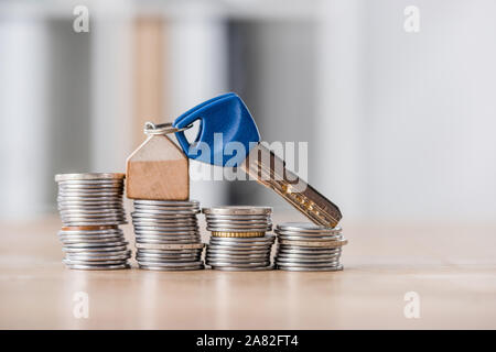 Schlüssel mit Spielzeug Haus Schmuckstück auf Stapel von goldenen und silbernen Münzen auf hölzernen Tisch Stockfoto