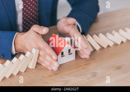 Der Risk Manager schützen Haus Modell von Domino Effekt der fallenden Blöcke mit Händen 7/8 Stockfoto
