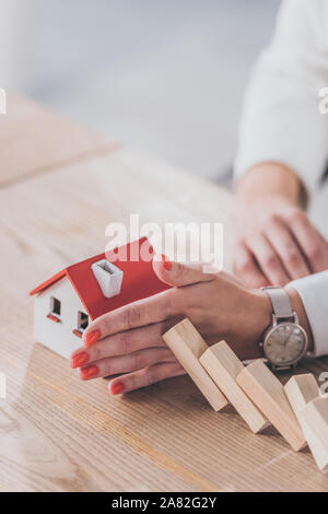 Teilweise mit Blick auf die Risk Manager schützen Haus Modell von sinkenden Holzblöcke mit Händen Stockfoto