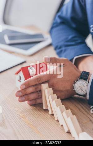 7/8-Ansicht von Risk Manager schützen Haus Modell von sinkenden Holzblöcke mit Hand Stockfoto