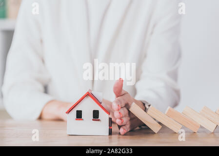 Teilweise mit Blick auf die Risk Manager schützen Haus Modell von sinkenden Holzblöcke mit Hand Stockfoto