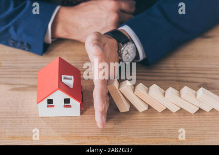 7/8-Ansicht von Risk Manager schützen Haus Modell von sinkenden Holzblöcke mit Hand Stockfoto