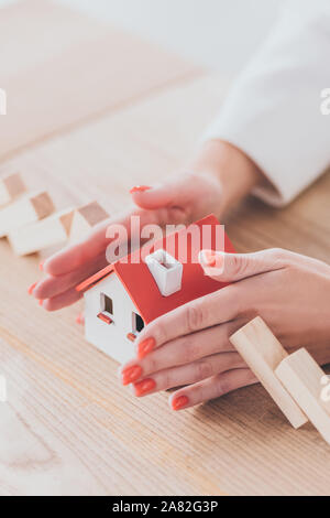 Teilweise mit Blick auf die geschäftsfrau Schutz Haus Modell von sinkenden Holzblöcke mit Händen Stockfoto