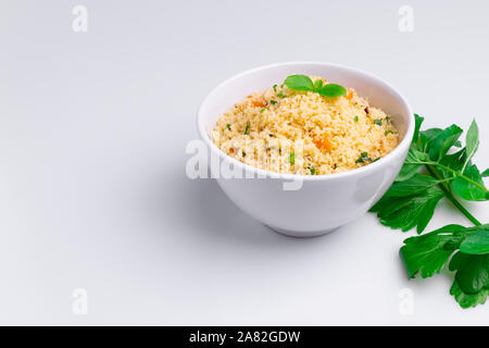 Leckere hausgemachte vegetarische Couscous mit Datteln, Rosinen, Petersilie, Tomate, Zitrone und Olivenöl in einer weißen Schüssel auf weißem Hintergrund, traditionelle Moro Stockfoto