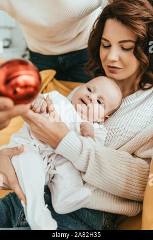 7/8-Ansicht von Vater übersicht Christmas Ball Cute Baby liegend auf Mütter Hände Stockfoto