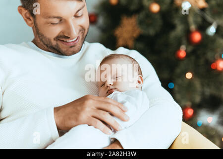 Lächelnd Vater Holding schlafendes Baby in der Nähe von Weihnachten Baum Stockfoto
