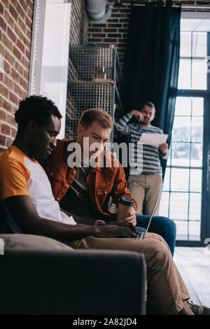 Nachdenklich afrikanische amerikanische Geschäftsmann mit Laptop beim Sitzen auf einem Sofa in der Nähe von Kollegen Stockfoto