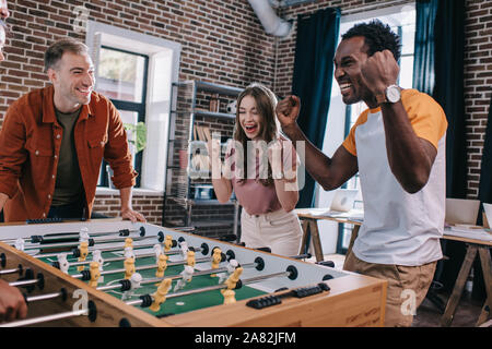 Aufgeregt multikulturellen Geschäftsleute zeigen Gewinner Geste beim Spielen Tischfußball in Office Stockfoto