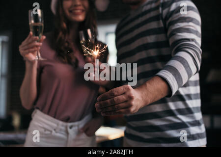 7/8-Ansicht der Geschäftsmann und Geschäftsfrau in santa Hüte auf Sparkler halten Sektgläser Stockfoto