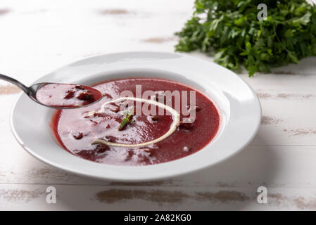 Leckere Rüben Suppe mit Sauerrahm in eine weiße Platte auf weissem Holztisch Hintergrund. Weiches Licht. Traditionelle ukrainische Russischen Borschtsch Rote-Bete-Suppe Stockfoto