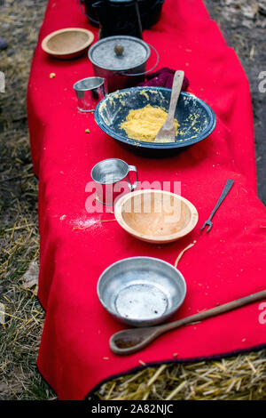 Rustikale Schüsseln und Töpfe sind, auf einem Tisch aus Strohballen, und ein blauer Emaille Schüssel zeigt ein getreidemehl Mischung für Johnny Kuchen Stockfoto