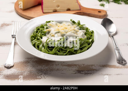 Hausgemachte greeen Spinat Bandnudeln mit béchamelsoße Soße in eine weiße Platte, rustikalen Holztisch Hintergrund, weiches Licht. Italienisches Essen Stil Stockfoto