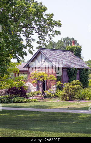Eine kleine Cottage liegt in einem schönen Garten, mit grünen Bäumen und Pflanzen und Klettern Efeu an den Wänden Stockfoto