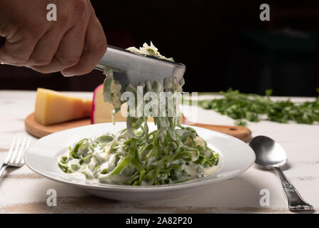 Hausgemachte greeen Spinat Bandnudeln mit béchamelsoße Soße in eine weiße Platte, rustikalen Holztisch Hintergrund, weiches Licht. Italienisches Essen Stil Stockfoto