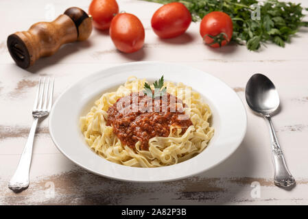 Fettuccine Pasta Bolognese mit Tomatensauce in eine weiße Platte auf rustikalen Holztisch Hintergrund, weiches Licht Stockfoto